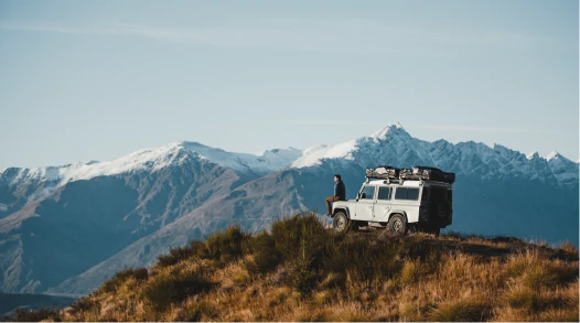 A man and a woman with a Land Rover overlooking hills in New Zealand.